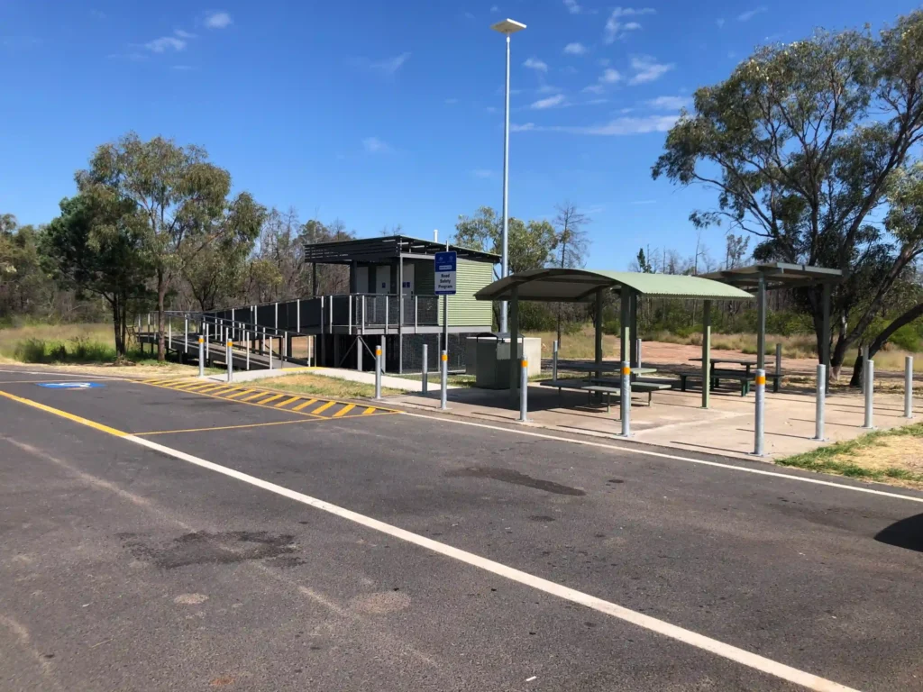 Raised Queensland TMR restroom with accessible ramp, two cubicles, storage room, and nearby shade structures.