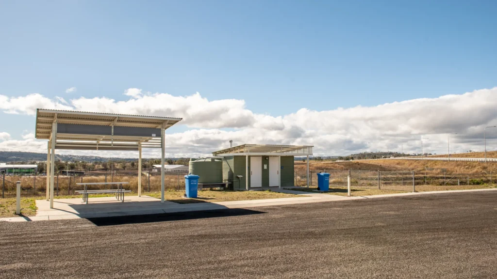 Wide shot of Toowoomba truck stop toilet facility with two cubicles and adjacent shade structure rest area.
