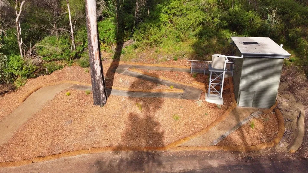 Rear view of Wonboyn toilet amenity at Myrtle Cove with water tank on a tank stand, set in bushland.