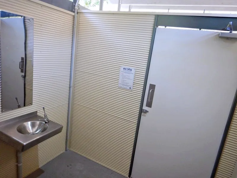 Interior of cubicle with lined walls, polished stainless-steel mirror, and handbasin.