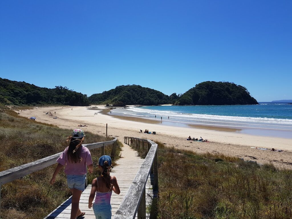 Matapōuri Beach with people sunbathing, swimming, and relaxing—busy day on the sand.