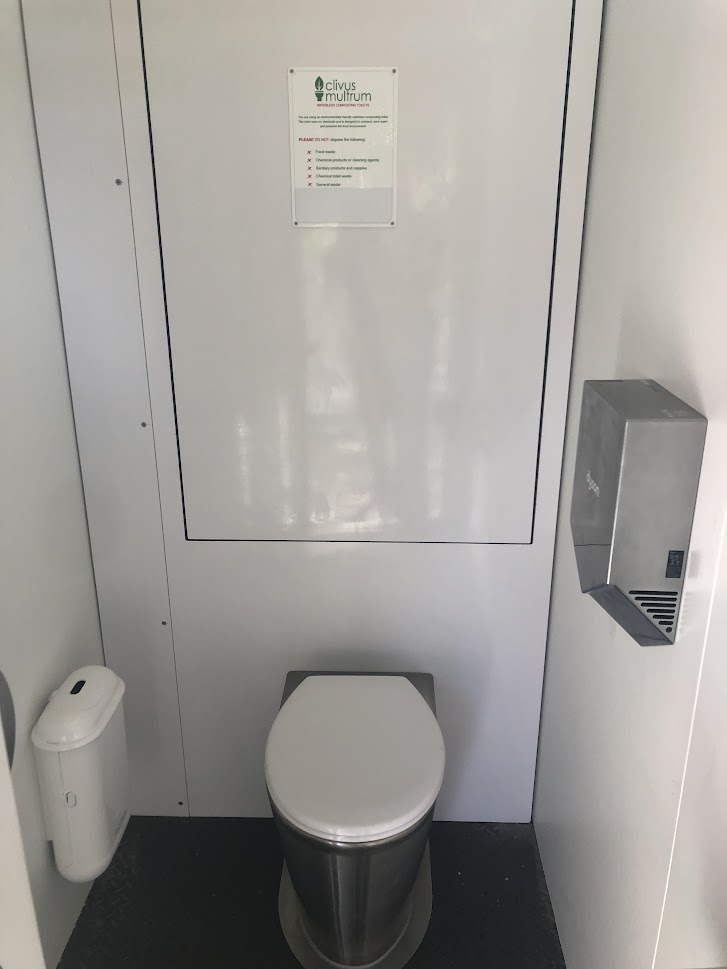 Stainless-steel toilet pan in cubicle with wall-mounted hand dryer and hygiene bin.
